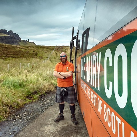 A close up of a Hairy Coo coach and tour guide with the Old Man of Storr in the background - Isle of Skye