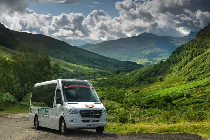 The Hairy Coo mini coach with scenic Scottish countryside in the background