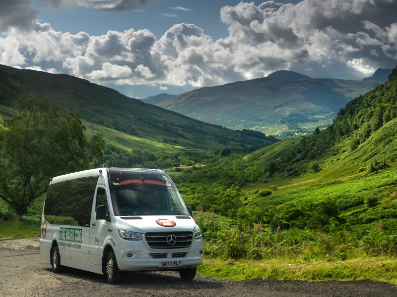 The Hairy Coo mini coach with scenic Scottish countryside in the background