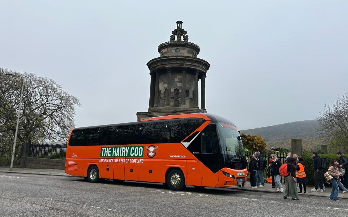 WhatsApp Image 2025-04-23 at 09.11.16_d4a76b22 A Hairy Coo orange coach at the new meeting point 1759 Regent Rd, Edinburgh EH8 8DR, in front of the Burns Monument