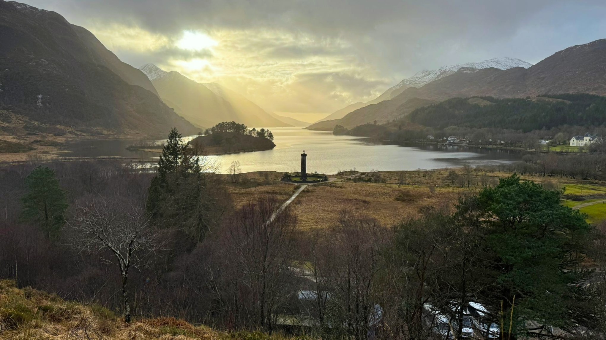 Glenfinnan Monument at the top of Loch Shiel with snow-capped mountains in the background.