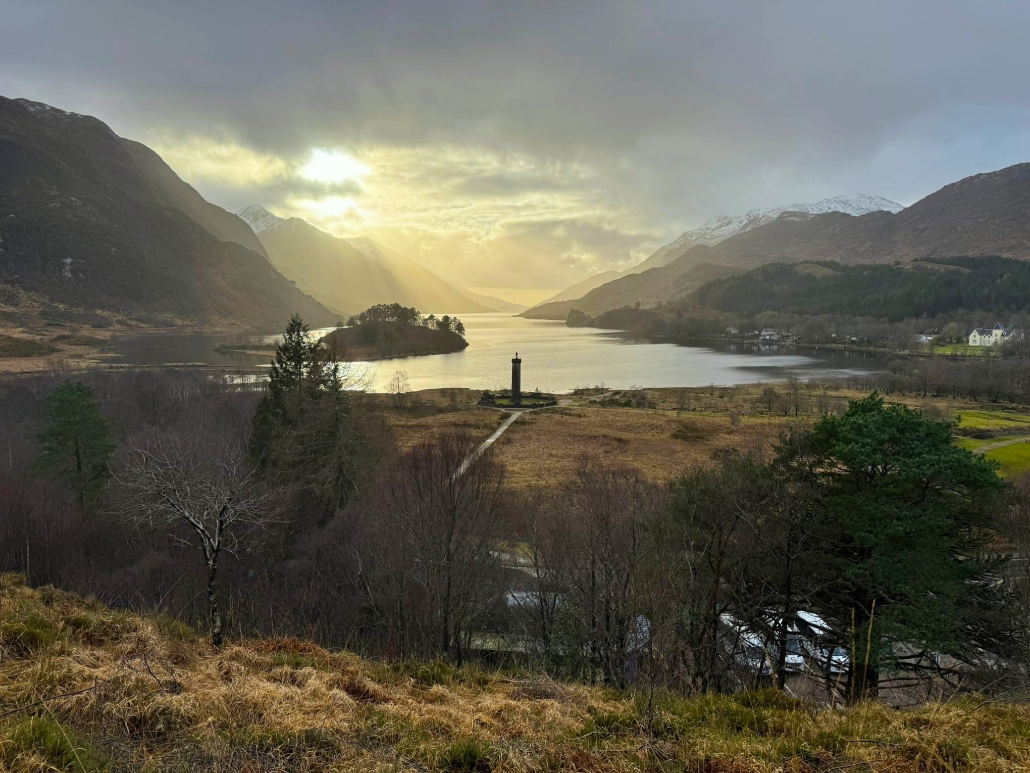 Glenfinnan Monument at the top of Loch Shiel with snow-capped mountains in the background.