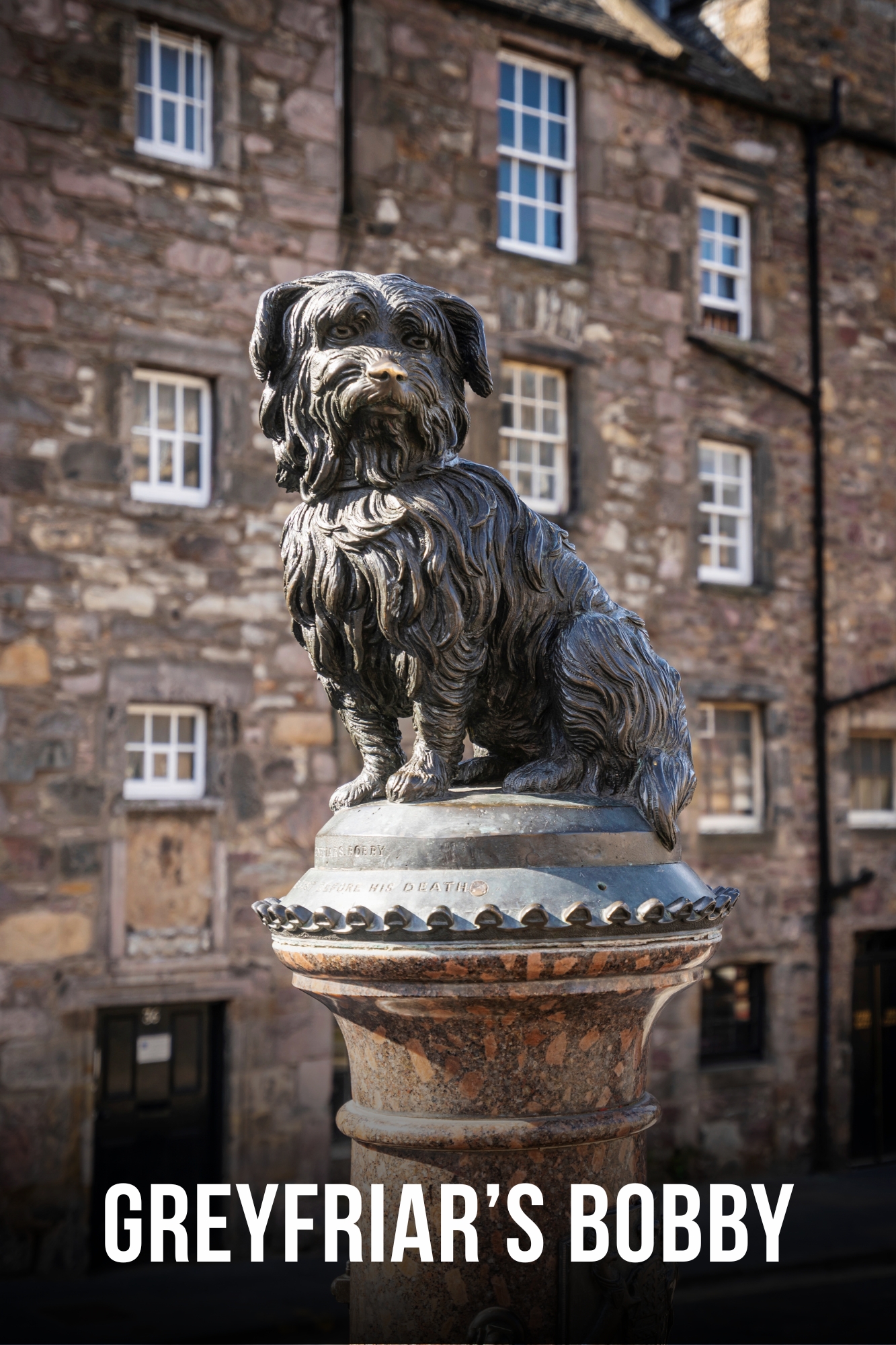 Statue of a dog on a pedestal with stone building in the background.