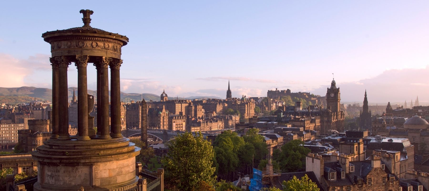 View of Edinburgh cityscape at sunset with a prominent monument in the foreground.